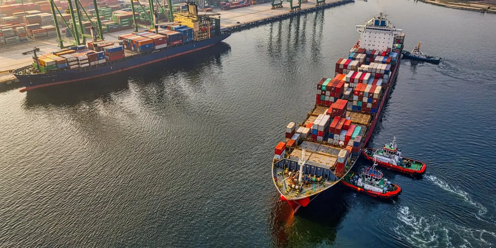 Ett containerfartyg på väg ut ur hamnen med bogserbåtar